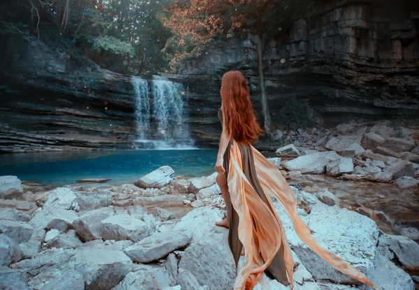 Charmante rothaarige Mädchen steht an der Küste des klaren, kalten klaren Sees, brillante magische Wasser des Wasserfalls in Georgien, Dame in langen grünen eleganten Flugkleid geht über Steine, Martyvili Canyon Natur — Stockfoto