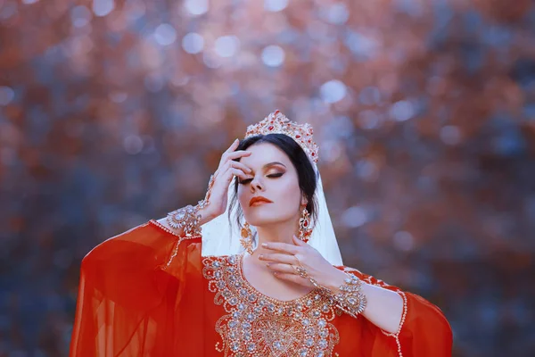 Шамаханська королева і приваблива темноволоса шейха в чудовій розкішній червоній сукні, багата східна наречена з золотими прикрасами, коштовностями і макіяжем, холодними кольорами, витончена дивовижна дама — стокове фото