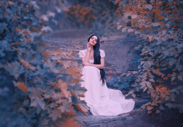 Deusa da floresta em degraus de pedra, sonhos com os olhos fechados, menina de cabelos escuros em vestido branco longo, coroa de ouro elegante em sua cabeça, o espírito de conto de fadas escuta o som da grama e folhas — Fotografia de Stock