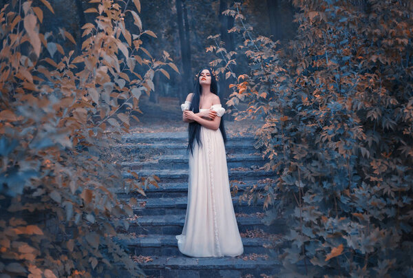 A marvelous, incredible Greek goddess of love, Aphrodite, descended to earth. Bliss and pleasure fill her soul. A young woman with long hair in a white dress is standing on an old staircase