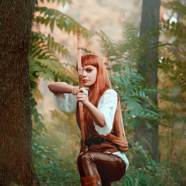 Neues Bild von Rotkehlchen als Jägerin, attraktive Dame in weißem Hemd und Lederhose zog Bogen vor Zielschuss, selbstbewusster Verdiener mit roten Haaren präpariertem Pfeil, helles Foto im grünen Wald — Stockfoto