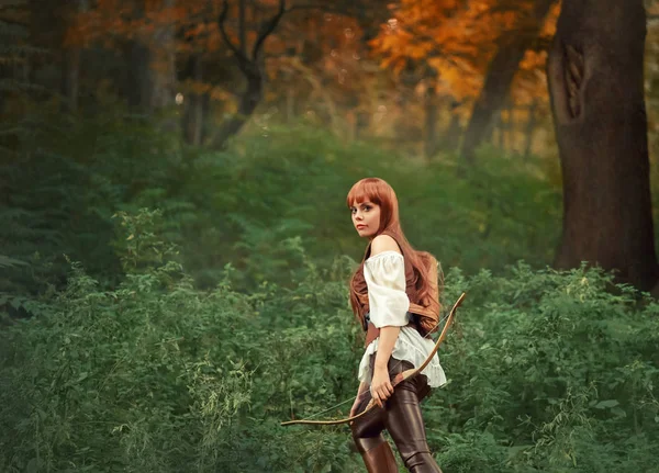 Image of forest hunter, attractive girl with long red hair in white shirt and leather pants goes hunting, holds wooden bow in her hand and quiver of arrows behind her back, kitsune in human form — 图库照片