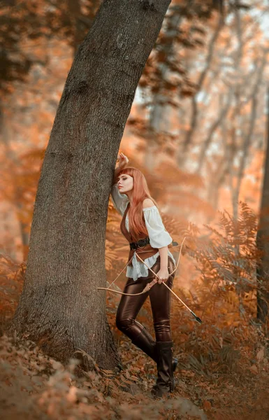 forest robber rests leaning against a tree in the autumn orange forest. a lovely girl with bright red hair holds a bow in her hand and arrows in the quiver behind her back, Lady Robin Good