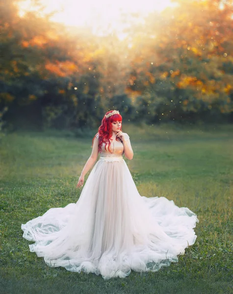 Bright art photo, cute large plump tender girl with red hair in long silver light dress with white train stands in middle of green meadow, new tale about Ariel, bride princess with diadem in sunlight — Stock Photo, Image