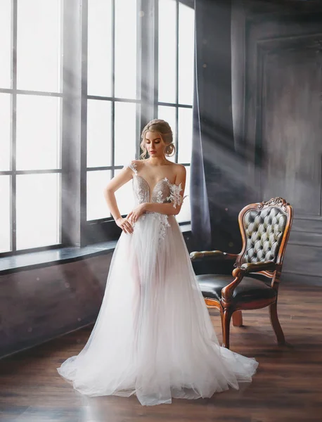 Charming excellent lady became bride, girl with blond gathered hair tries on wedding chic white luxurious light dress in spacious room with large windows and bright light, naked gentle shoulder — Stock Photo, Image