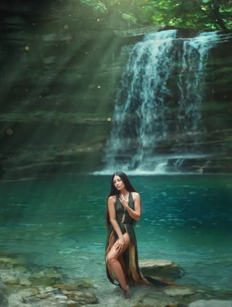 Magia de la naturaleza tropical, de pelo oscuro sexy chica sale de la clara cascada transparente azul del agua del lago, ninfa de mar en vestido verde con escote profundo. Sirena en los rayos del sol. Fotografía artística — Foto de Stock