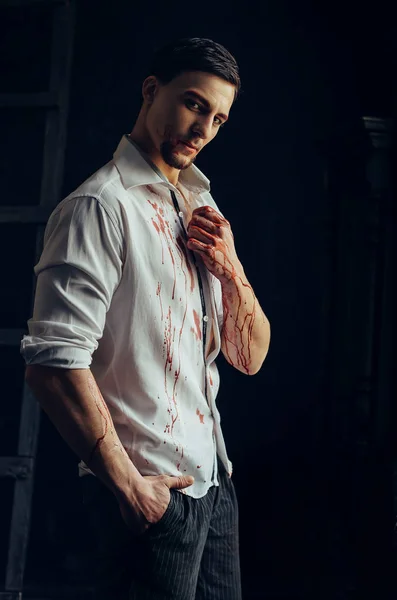Hot sexy man with dark hair and eyes, guy in white bloody shirt, flowing red blood on hands, chest and chin, attractive vampire and servant of devil and Satan, passionately looks straight into camera — Stock Photo, Image