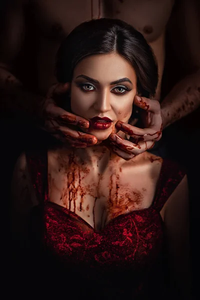 Szép büszke hölgy, piros ruhás, a kísértés előtt az ördög, a hölgy tartja a kezét, vér áramlik át a kéz, profi sminkes, nyakán véres történet a vámpírok — Stock Fotó