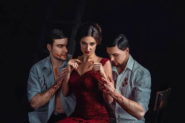 Bela senhora orgulhosa em vestido vermelho em tentação diante do diabo seus braços em sangue, fluindo através das mãos, artista de maquiagem profissional, história sangrenta de vampiros, dois homens quentes sexy e uma mulher — Fotografia de Stock