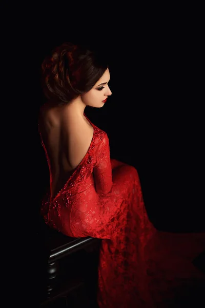 Belle dame fière en tentation devant le diable, maquilleuse professionnelle, histoire sanglante de vampires, magnifique robe longue rouge aux épaules ouvertes, assise dos à la caméra, cheveux foncés réunis — Photo