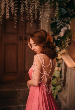 Güzel ince kız uzun güzel ince elbise, şaşırtıcı Pembe çiçek Prenses, bir çocuk gibi yetişkin kız ateşli Kızıl saçlı, Bayan geri kamera için rahat yumuşak atmosferde inciler ile dekore edilmiş giysi