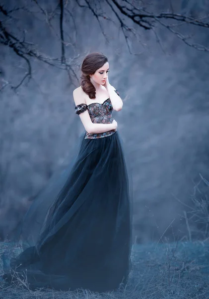 Gorgeous attractive brunette, lady in a long black dress with bare open arms and shoulders, the girl alone in the autumn cold forest, the weather in November is a dark princess in the form of raven — ストック写真