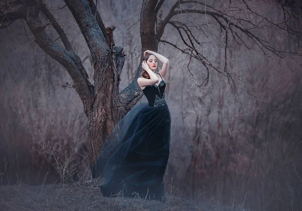 Incrível morena macia, senhora em um vestido preto longo com braços e ombros abertos nus, a menina sozinha na floresta fria de outono, o tempo em novembro é uma princesa escura na forma de corvo — Fotografia de Stock