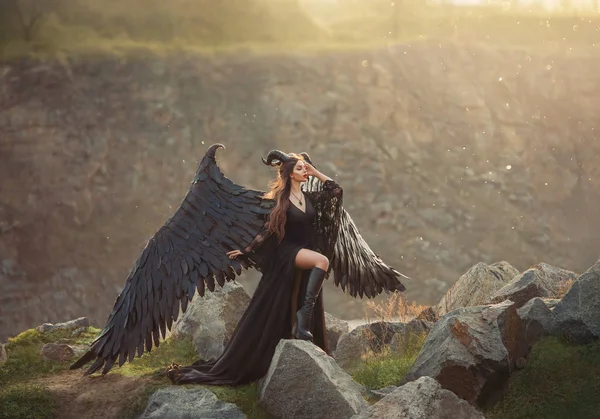 Misteriosa senhora em vestido de renda luz preta com trem longo, menina com perna aberta em botas de couro, anjo de chifre escuro do céu, mensageiro da morte com grandes asas na borda com olhos fechados em raios de sol — Fotografia de Stock