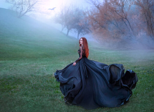 Mysterious girl with red hair runs from forest in gorgeous lace royal dress with flying light long train, lady in green frozen meadow and fog, sorceress turns to black crow and flies to sun.