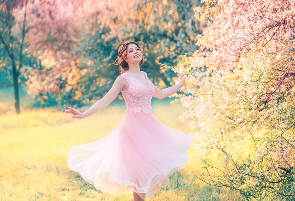 Menina feliz em curto voo vestido rosa suave ri alegremente, boneca princesa gira em jardim de primavera amarelo brilhante com árvores floridas, emoções positivas, movimento na foto com cores criativas — Fotografia de Stock