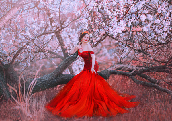 Charming nymph sits on fallen tree in spring forest, lady in gorgeous red scarlet long dress with bare shoulders, mermaid becomes human , fairy-tale princess walks in sakura garden, creative colors.
