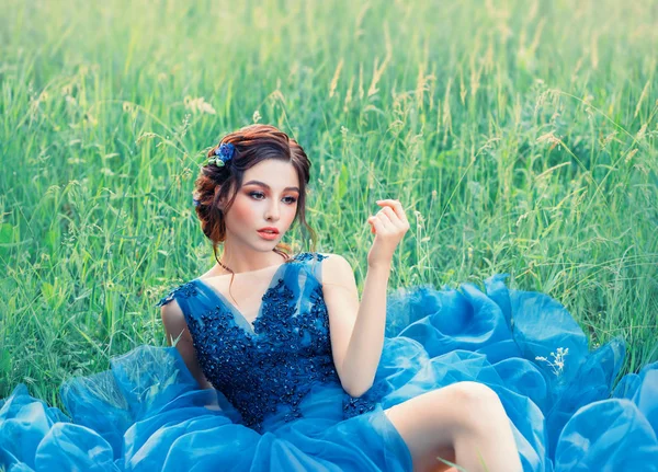 Affascinante storia misteriosa sulla bambola di porcellana, bella ragazza in abito lungo blu lussureggiante delicato. signora con capelli scuri intrecciati e trucco delicato, pelle perfetta, fiore in erba verde sulla natura fresca — Foto Stock