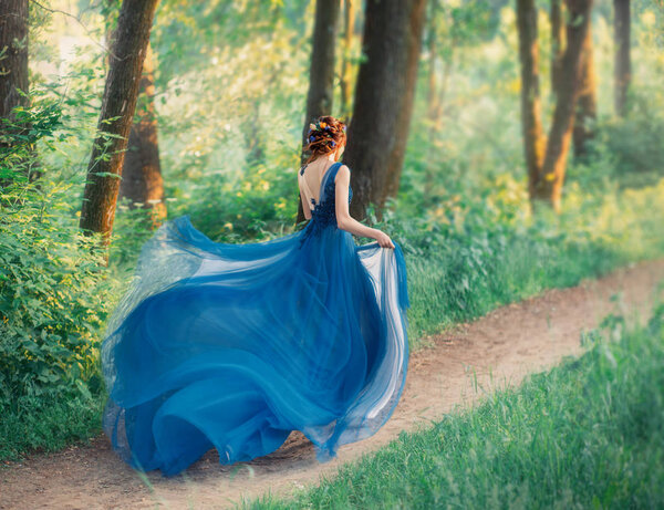 Mysterious girl with red braided hair runs off from royal holiday, lady in long elegant blue dress with flying light train like flower, the magical transformation of beautiful woman during sunset.