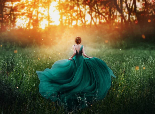 Волшебная картина, девушка с рыжими волосами бежит в темный таинственный лес, дама в длинном элегантном королевском дорогом изумрудно-зеленом бирюзовом платье с летающим поездом, удивительное преображение во время огненного заката — стоковое фото