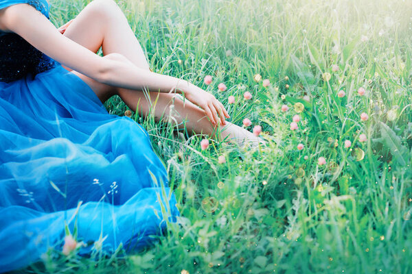 charming delicate art photo with creative colors, the lady touches the fingers of the hand of her sexy bare legs, the princess in a long blue lush chic elegant dress, free space for text, no face