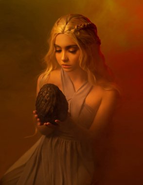 sarışın örgülü saçlı gizemli bayan eski bir vintage elbise karanlık bir odada oturuyor, kız korkunç bir büyük dikenli yumurta tutuyor, beklenmeyen bulmak, insan ellerinde efsanevi yaratık