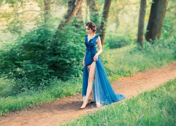 The girl in the evening, luxurious, watercolor dress, with a high slit. long legs. The image of the party, a young charming graduate. Collected hairstyle with weaves, hair decorated with blue flowers — Stock Photo, Image