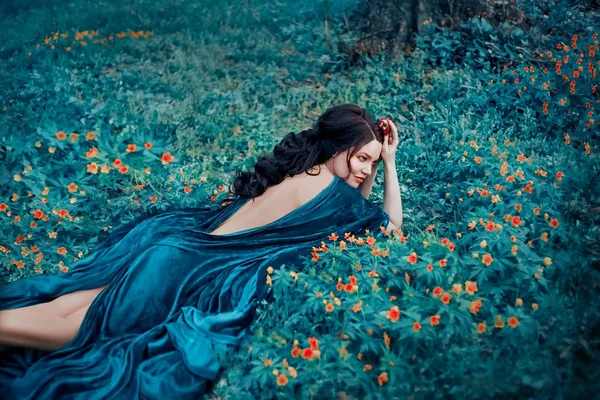 Bruxa sedutora em um manto azul de veludo descansando em uma clareira com flores amarelas. Cabelo escuro longo deitado em uma nua, aberto para trás. Tecido luxuoso, caro e brilhante. Rainha da floresta . — Fotografia de Stock