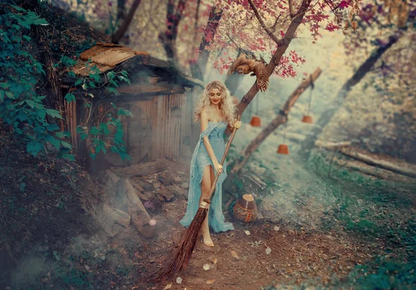 良い魔術師、シンデレラの妖精のゴッドマザーは、森の中に隠された彼女の小さな家の中庭を掃除しながら踊り、歌います。シンプルでボロボロの古いグレーのドレス。カーリー, ブロンドの髪 — ストック写真
