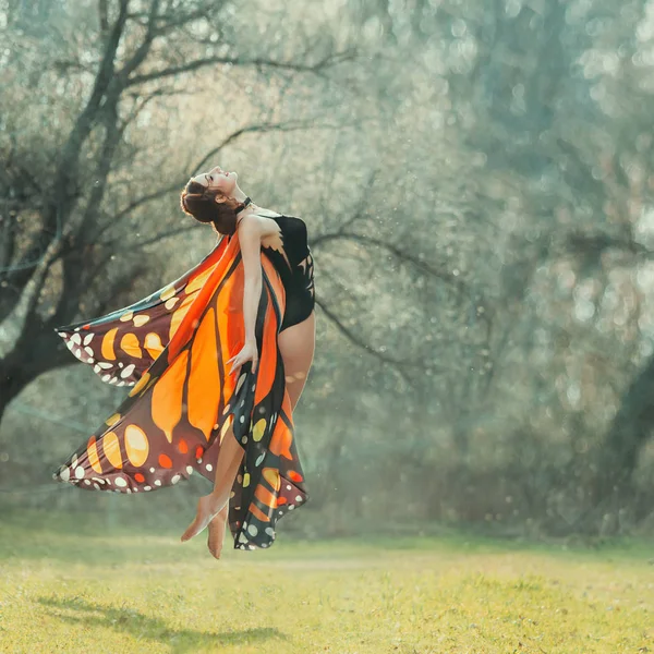 Atrakcyjna smukła dziewczyna z plecionych ciemnych włosów w czarnym eleganckim ciele i lekkie skrzydła motyl leci w powietrze, radość z ciepłych letnich dni, pierwszy lot ćma, lekkość i wdzięk — Zdjęcie stockowe