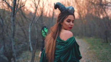 diğer dünyanın kraliçesi, kafasında büyük siyah boynuzları ile kız, açık omuzlu uzun, şaşırtıcı yeşil velor bornoz giymiş, bir abyss yol açar. sihirli personel ile vampir gizemli görüntü