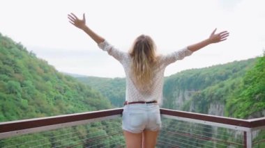 rahat giysiler içinde sarı saçlı mutlu bayan kamera geri ile duruyor, yüzü olmayan genç ince kız ellerini yukarı çeker, turist neşeyle ve sevinçle dağlarda bağırır, kuş gibi uçmak istiyor