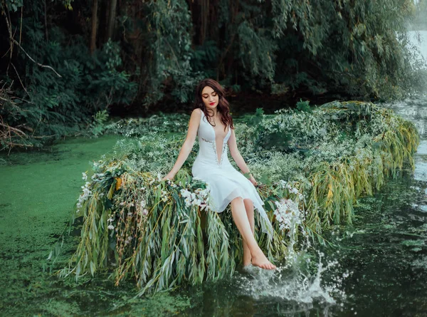 Vrolijke vrouw in een witte vintage outfit zit op een boot en spat haar blote voeten in het water. wilde achtergrond rivier met waterlelies en groene bomen. Gelukkige vrouwelijke prinses diepe hals jurk — Stockfoto