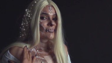 Beyaz saçlı şeytan ve yüzü boyalı kafatası karanlık gizemli odada neşe içinde gülümseyen, eski moda giyinmiş ölü kız, çıplak omuzlu kadın vücuduna bakıyor, ölü ruhları kutluyor