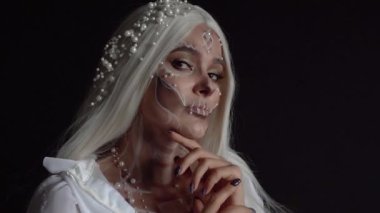 Stüdyo portresi, siyah duvarlı bir odada hoş bir inci kafatası makyajı yapan bir kızın, Cadılar Bayramı sonbahar partisi için ölü bir gelinin resmi, gelinlik içinde uzun düz beyaz saçlı bir kadın.