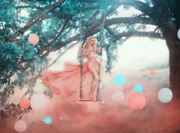 艺术公主小精灵站在神奇的森林摇曳着神秘的树。穿着粉红长裙的女仙女飘扬着飞舞的飞舞风.幻想的自然白色蓝色球，气球。红色浓雾彩烟. — 图库照片