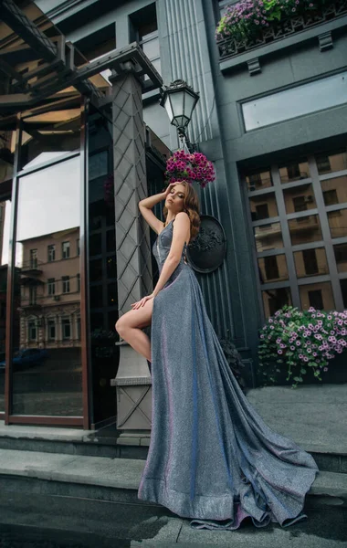 Мода красива молода чарівна жінка позує модель на тлі сучасної сірої будівлі, розквітнуть квіти. Модна ретро зачіска Голлівудська хвиля. Гола сексуальна нога. Довга вечірня елегантна сукня. вечірка випускного зображення — стокове фото