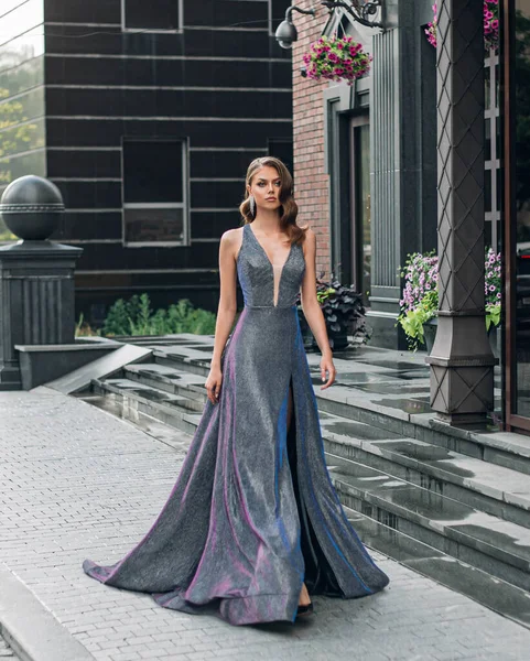 Bella giovane moda splendida donna passeggiate, moderno edificio nero, gradini di granito. Bruna ragazza acconciatura Hollywood onda stile retrò. Abito lungo sera grigio lusso glamour iridescente lucido elegante — Foto Stock