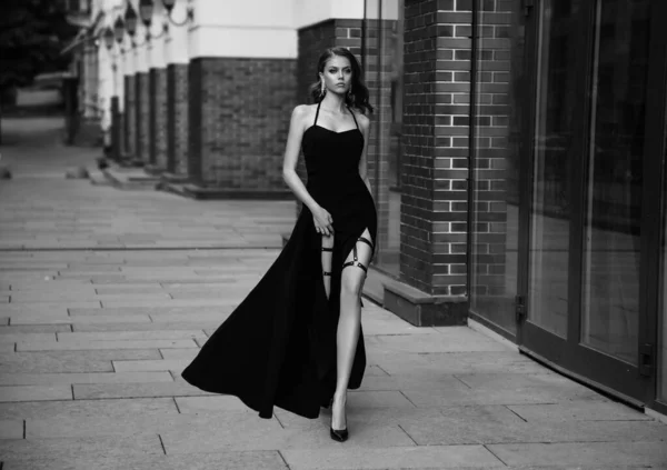 Vysoká móda. Sexy dívka v klasických večerních šatech. Černobílá fotka. Luxusní veteránka s dlouhou holou nohou. Krásná retro dáma. Královna krásy. Noir styl elegantní model procházky po staré městské ulici — Stock fotografie