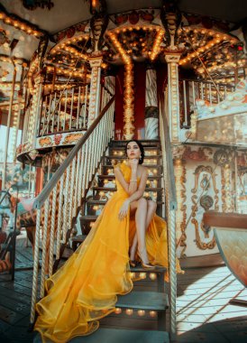 Açık sarı gece elbisesi içinde merdivenlerde oturan genç ve güzel bir kadın. Bir lunapark ve atlıkarıncada poz veren manken.