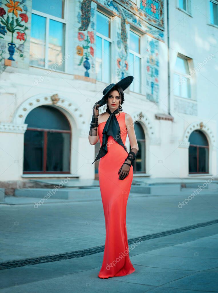 Fotos de Elegante dama retro en un vestido largo de glamour rojo noche.  Joven mujer de moda con estilo en un sombrero negro con ala ancha y guantes  de tul alto. arco