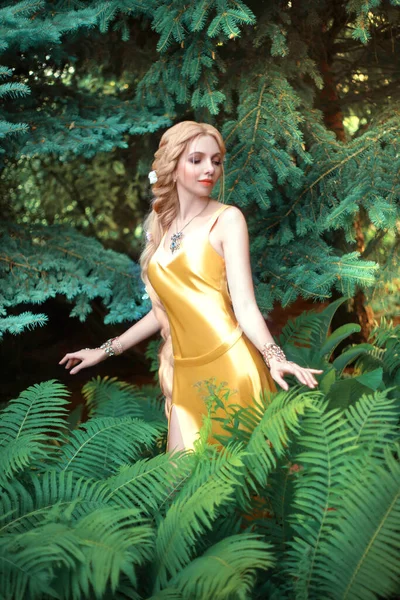 Saçları çok uzun ve örülmüş güzel sarışın bir kadın. Kız baştan çıkarıcı sarı bir elbise giyiyor. Yeşil yaz bahçesinin arka planında poz veren manken.. — Stok fotoğraf