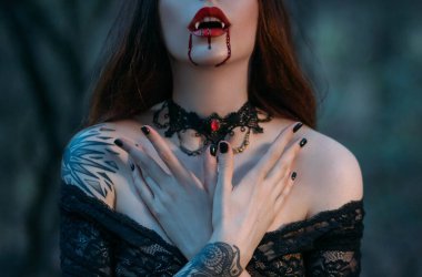 Yüzünün silueti keskin dişleri olan çekici seksi vampir kadın kırmızı dudaklarına kan damlaları damlatıyor. Güzel ağzın yakın plan portresi. Şenlikli sanat makyajı. Boynunda gotik dantel boğucu var.