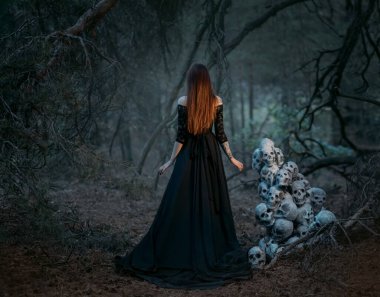Siyah, eski, uzun elbiseli hayalet bir kadının gizemli silueti. Gotik putperest kadın birçok ölü insanın kafatasının yanında. Vampir karanlık, gizemli bir ormanda yürüyor. Arka arkaplan