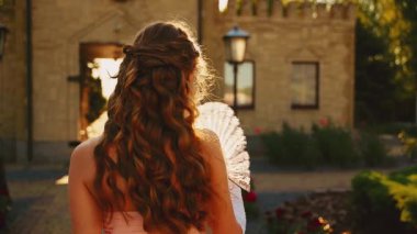 Manken pozu, ortaçağ bayan mutlu prenses el sallayarak yelpaze tutuyor. Fantezi kadın seks kraliçesi arkasına bakıyor, beyaz uzun eldivenler giyiyor eski tarz şehir güzeli gülümseyen surat 4K