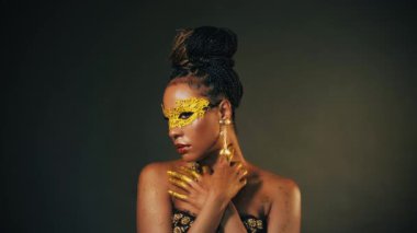 Gürültülü video. Portre Afrikalı kadın altın karnaval maskesi takmış. Kız model mükemmel cilt, akşam makyajı, pırlanta elmas taşlar dudak parlatıcısı, altın rengi boyalı eller