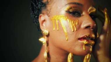 Yakın plan güzellik sanat portresi fantastik profesyonel makyöz Afrikalı kadın, dudakları boyayla kaplı eller sıvı altın düşürür. Moda mankeni seksi yüz tanrıçası. Parlak gölgeli gözler sihirli parlaklıklar