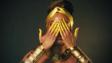 Gürültülü video. Fantezi sanat portresi, yakın plan, Afro-Amerikan kadın yüzü. Altın metalik makyaj gözleri, parlak gölgeler dudak parlatıcısı. Altın boyalı eller. Model kız. Siyah Stüdyo
