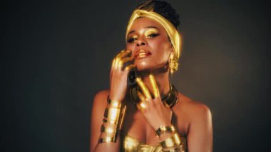 Portre Güzel fantezi Afrikalı mutlu kadın gülümseyen yüz farı altın rengi boya. Altın makyaj sıvısı, parlak altın cilt. Model kız. Küpe takan Arap sarığı. Altın takı takıyor. 4K.