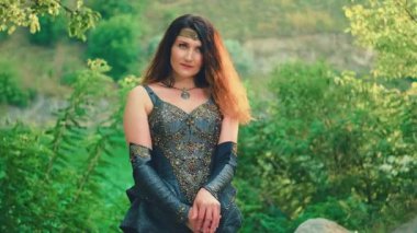 Fantezi kadın savaşçı elinde silah kılıcıyla savaşa hazır bekliyor. Savaşçı bayan eski tarz seksi kraliçe kızıl saçlı. Deri elbise, siyah zırh takımı. Yeşil yaz ağaçları orman güneşi 4k